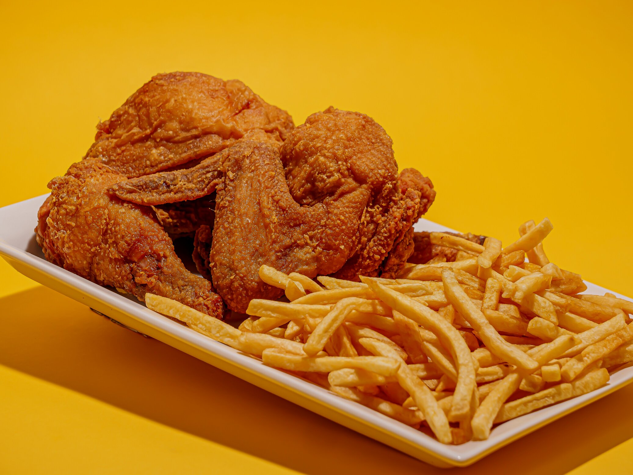 Close Up Photo of Fried Chicken and French Fries on Yellow Background